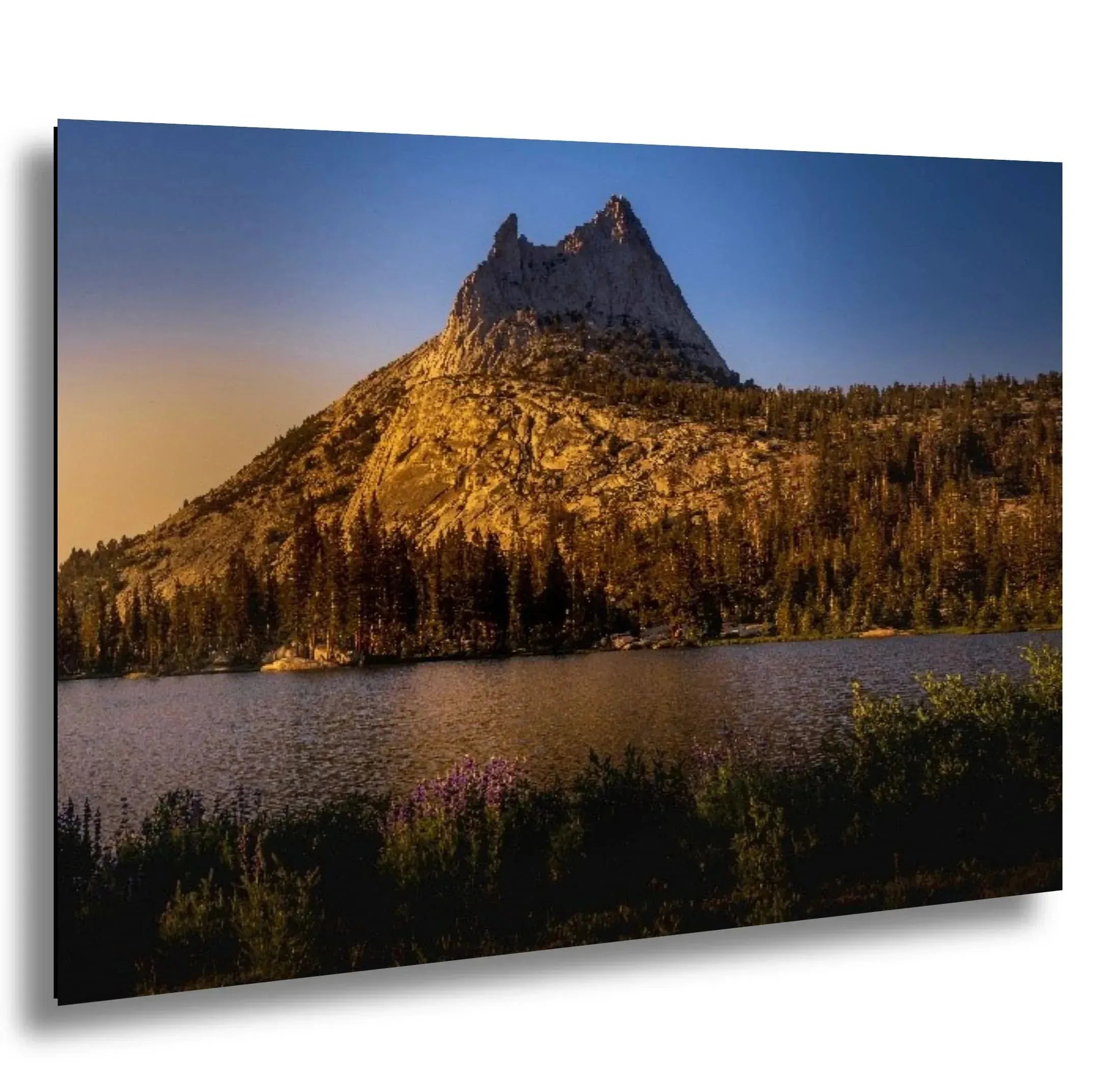 Golden mountain peak with surrounding pine trees and colorful wildflowers at the base, reflected in the calm lake during sunset.
