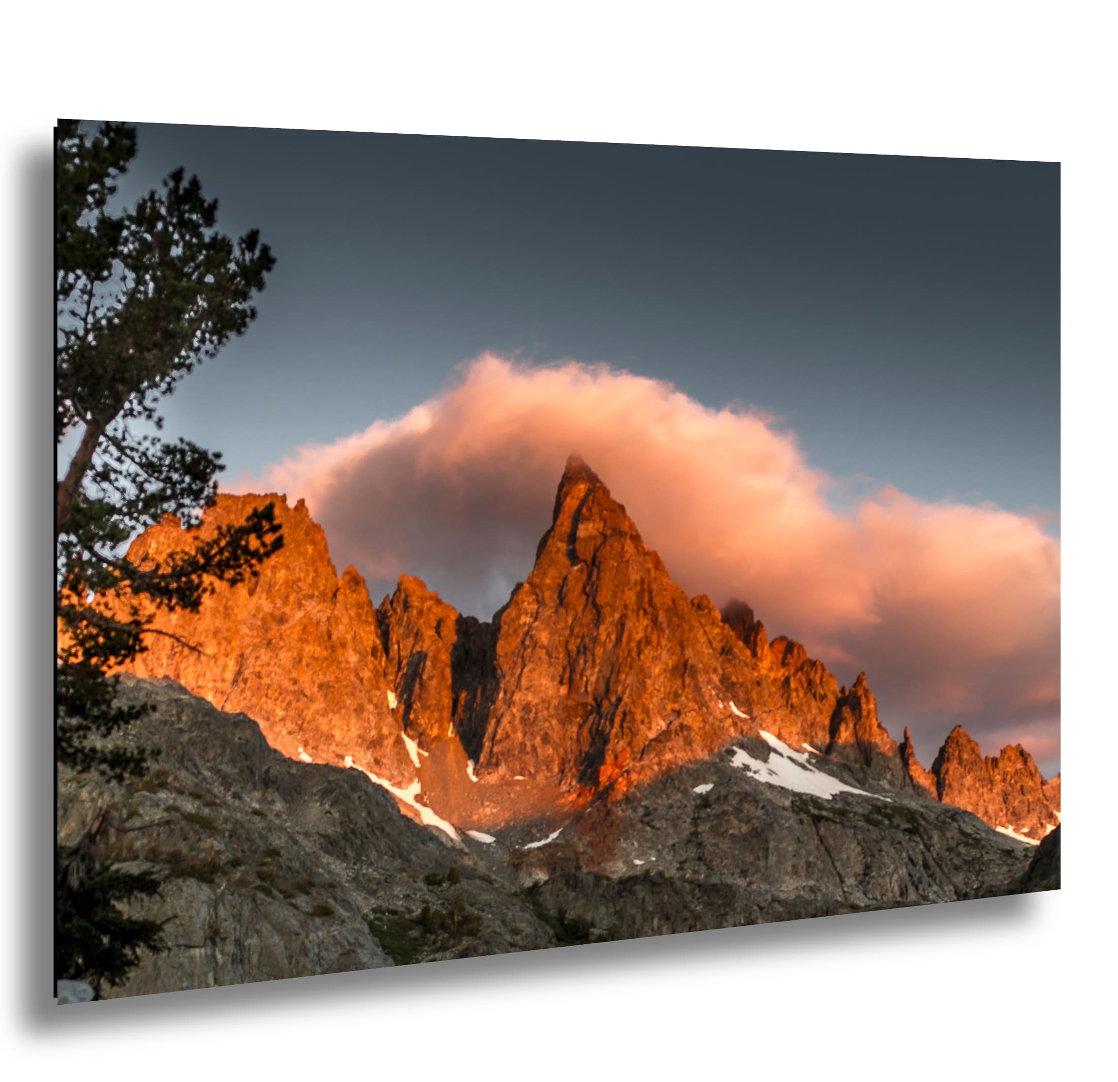 Close-up view of a mountain peak bathed in golden light with a soft cloud above, framed by trees on the left.