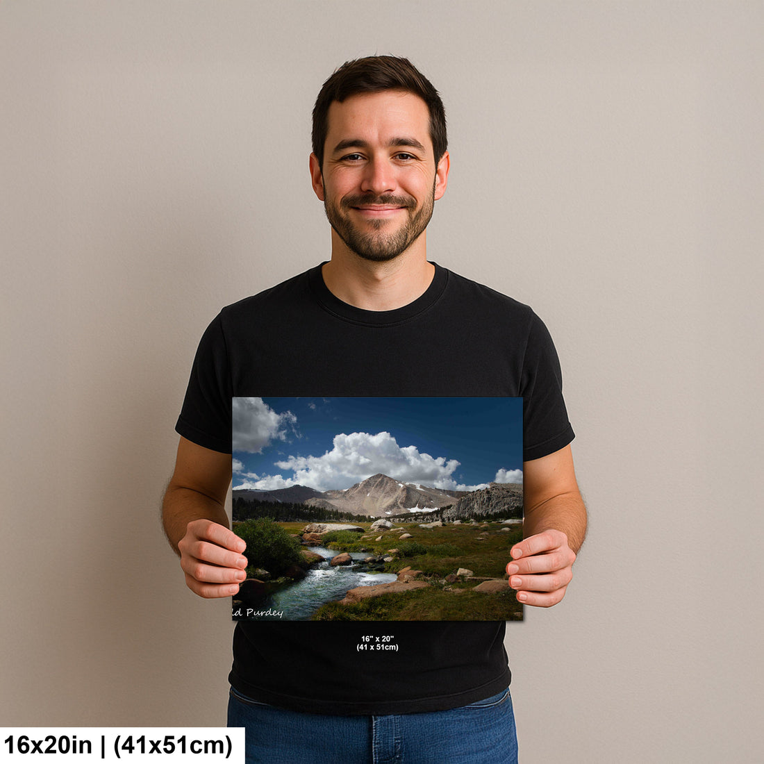Man holding alpine mountain stream and meadow landscape photography print with granite peaks and blue sky.