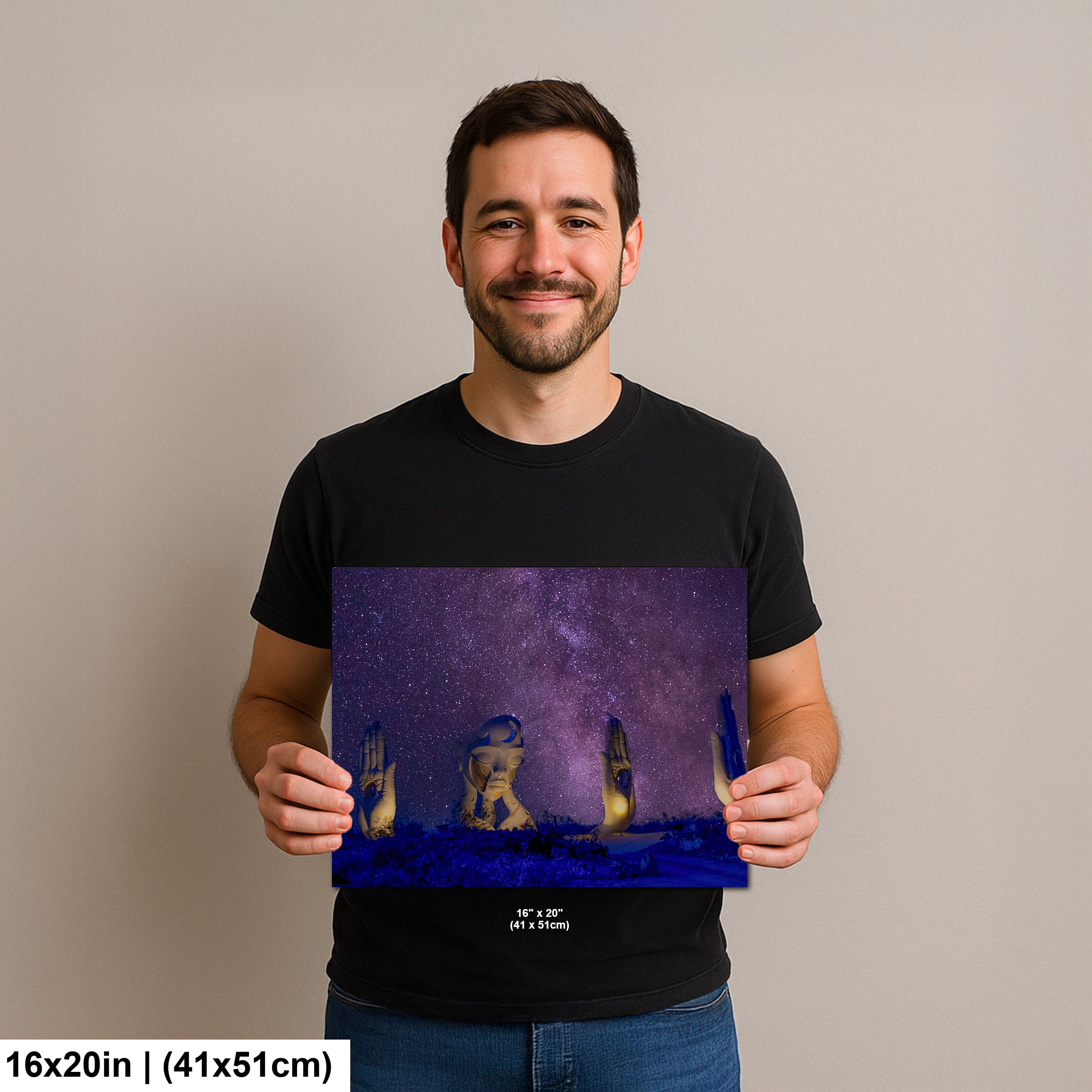 Man holding a 16x20 inch print of surreal sculptures under a starry sky, featuring a giant woman’s face and hands illuminated in a desert landscape.