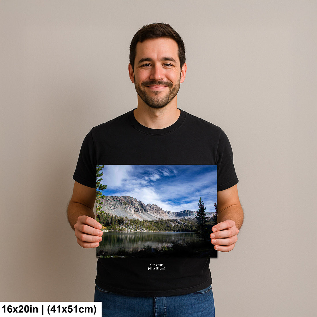Man holding snow-capped mountain and alpine lake landscape photography print with forest and blue sky.