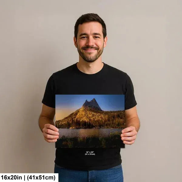 Man holding a 16x20 inch print of a serene mountain landscape with a tranquil lake, surrounded by trees and bathed in soft sunset light.