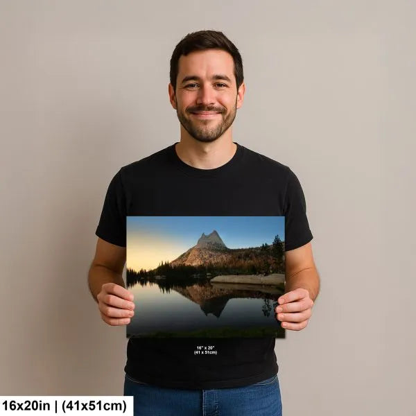 Man smiling and holding a 16x20 inch print of a mountain reflection in a peaceful lake surrounded by trees, with warm sunset lighting.