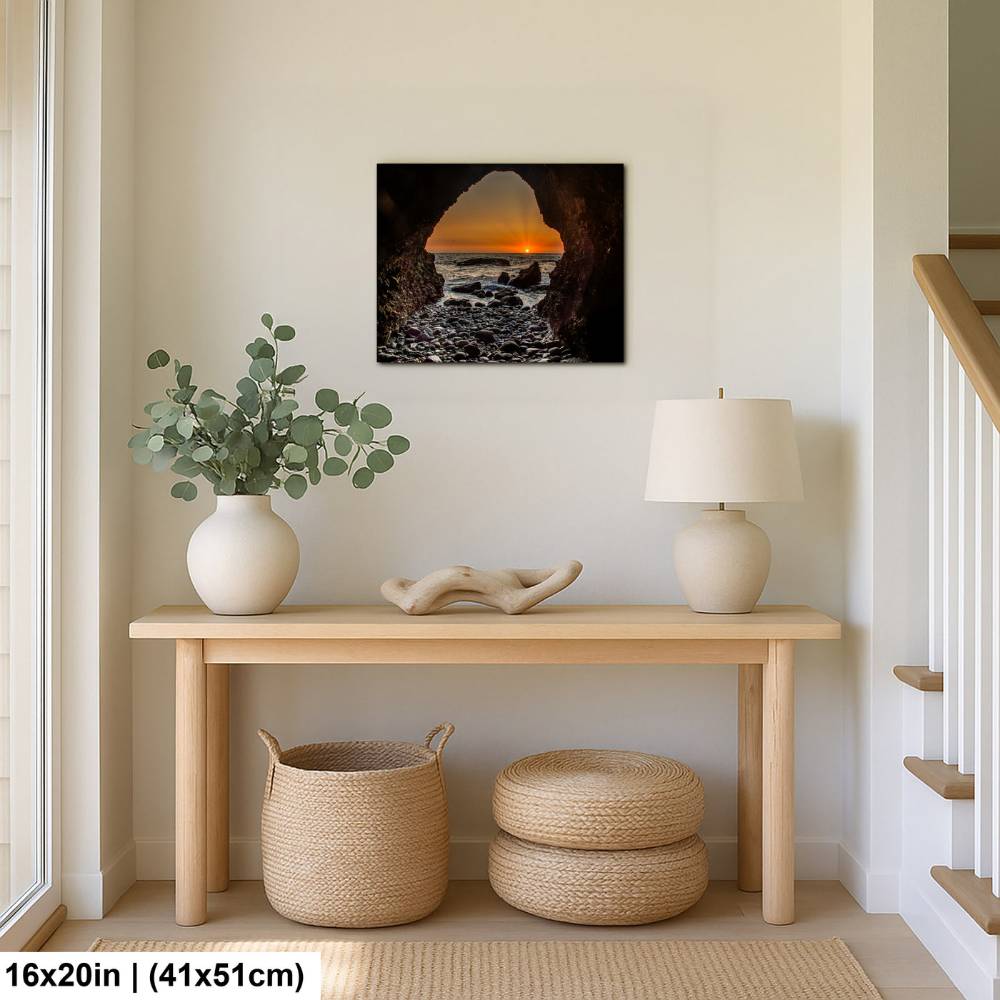 Modern entryway with a wooden console table, potted plant, and decorative items, featuring a sunset beach view through a rocky cave print on the wall.