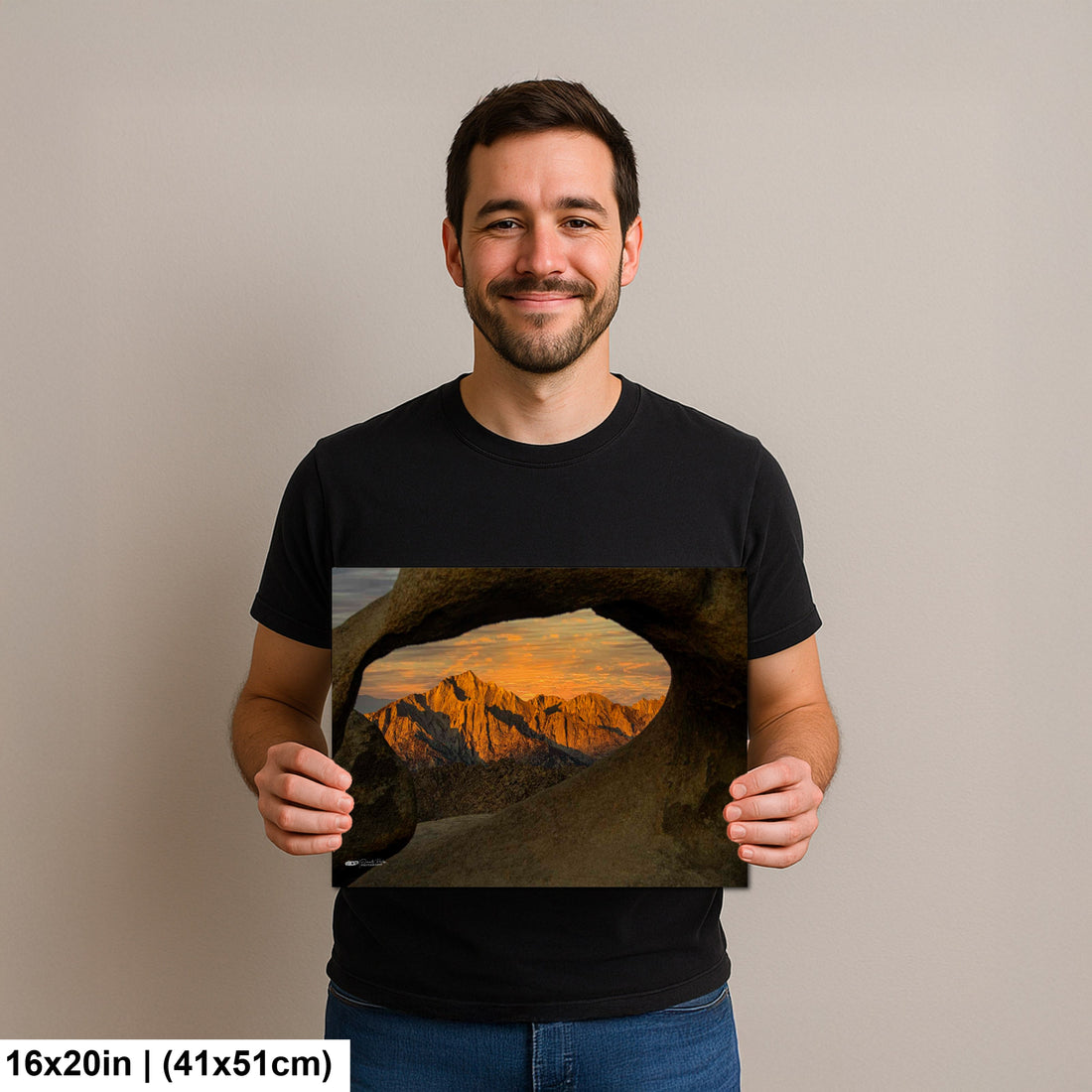 Man holding Joshua Tree sunset framed through granite rock window landscape photography print with golden peaks.