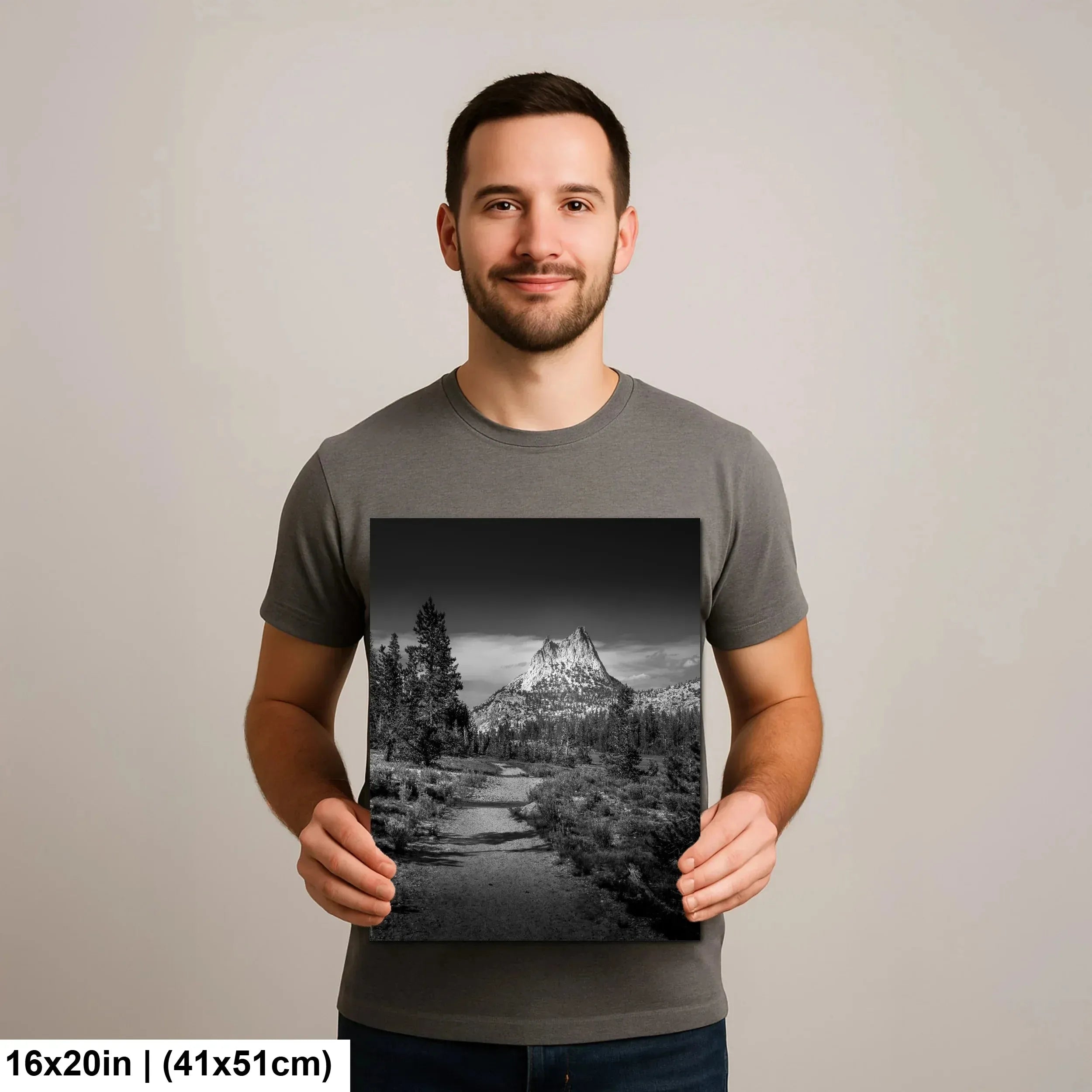 Man holding black and white mountain peak and stream landscape photography print with forest.
